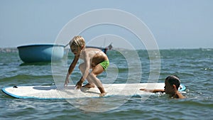 Little children enjoying sea surfboarding and waving hands in slow motion