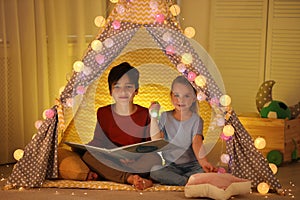 Little children with flashlight reading book in play tent