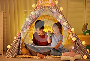 Little children with flashlight reading book in play tent