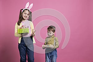 Little children holding handmade basket with painted eggs on camera