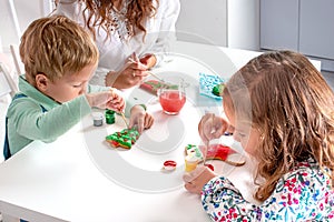 Little children with a nanny  to prepare for Christmas.  They sit at the table in the room photo