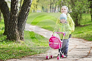 Little children play in yard with children`s toy doll for dolls. boy and girl play game of children playing stroller in courtyard