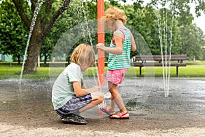 Little children playing at water splash pad fountain in park playground on hot summer day