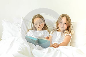Little children reading book in bedroom at home