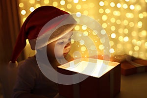 Little Christmas girl in a Santa hat looks into a magic gift box. Background color of the defocus. The concept of