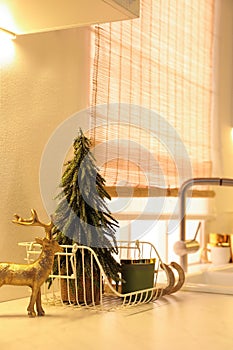 Little Christmas tree, candle and decorative reindeer on countertop in kitchen