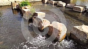 Little city creek with calm flowing water in slow motion through rocks in water under little bridge in summer in european city wit