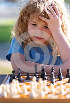 Little clever boy thinking about chess. Little boy playing chess outdoor in park. Close up face of clever smart child.