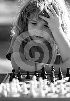 Little clever boy thinking about chess. Little boy playing chess outdoor in park. Close up face of clever smart child.