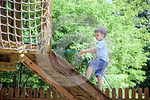 Little climber takes the rope bridge. Boy has fun time, kid climbing on sunny warm summer day