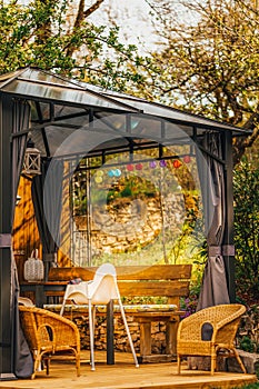 Little colorful lampions hanging on a pavilion in a garden on a sunny summer day. Cozy Chairs and Table standing underneath it