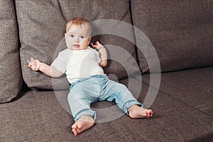 Little contented happy baby boy with pacifier sitting on a bed or a sofa. The only child in family