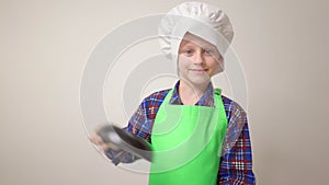 little cook boy in green apron and chef's hat stands with small frying pan in his hand and he waves it away. idea of