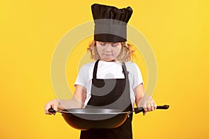 Little cook with cooking pan. Kid chef cook, studio portrait. Children cooking. Kid boy with apron and chef hat.