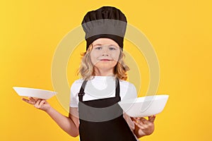 Little cook with cooking plate. Child chef cook. Child wearing cooker uniform and chef hat preparing food, studio