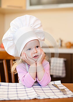 Little cook girl sitting at kitchen table waiting