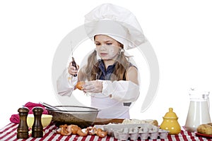 Little cook girl in a white apron breaks eggs in a deep dish