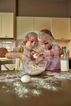 Little cooks. Adorable little children, boy and girl in aprons looking focused while preparing dough together on the