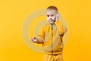 Little cool kid boy 3-4 years old in yellow clothes talking on mobile phone isolated on orange wall background, studio