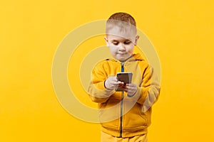 Little cool kid boy 3-4 years old in yellow clothes talking on mobile phone isolated on orange wall background, studio