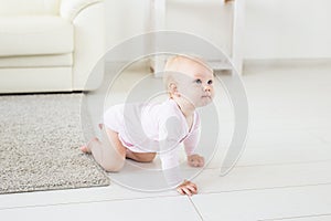 Little crawling baby girl one year old crawling on floor in bright light living room smiling and laughing. Happy toddler