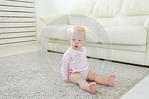 Little crawling baby girl one year old sitting on floor in bright light living room smiling and laughing. Happy toddler