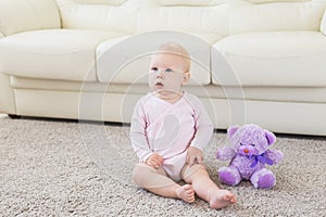 Little crawling baby girl one year old sitting on floor in bright light living room smiling and laughing. Happy toddler