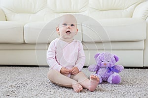 Little crawling baby girl one year old sitting on floor in bright light living room smiling and laughing. Happy toddler