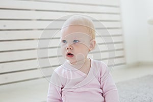 Little crawling baby girl one year old sitting on floor in bright light living room smiling and laughing. Happy toddler