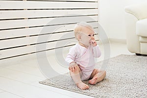 Little crawling baby girl one year old sitting on floor in bright light living room smiling and laughing. Happy toddler