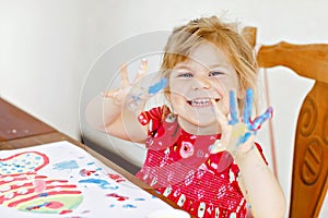 Little creative toddler girl painting with finger colors a fish. Active child having fun with drawing at home, in