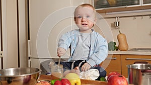 Little crying baby boy trying eating porridge with spoon on kitchen. Concept of healthy nutrition,diet and children food