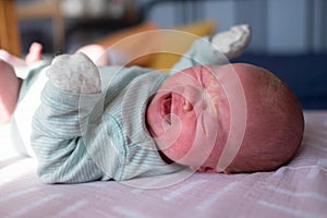 Little crying caucasian newborn baby on her bed suffering from colic