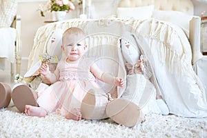 Little crying girl sitting between toy rabbits near bed