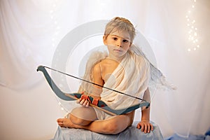 Little cupid toddle boy, holding bow and arrow, beautiful blond cherub