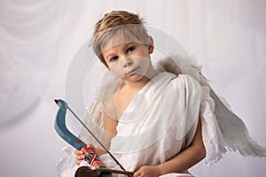 Little cupid toddle boy, holding bow and arrow, beautiful blond cherub