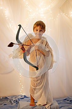 Little cupid toddle boy, holding bow and arrow, beautiful blond cherub