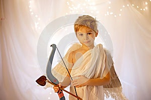 Little cupid toddle boy, holding bow and arrow, beautiful blond cherub