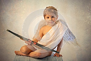 Little cupid toddle boy, holding bow and arrow, beautiful blond cherub photo