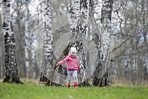 A little curly baby in a pink jacket and boots fun runs in the spring forest. The first flowers. Gentle symbol of spring