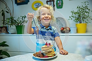 Little curly boy eating sweet pancakes