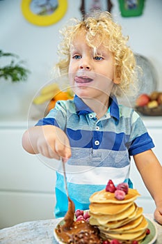 Little curly boy eating sweet pancakes