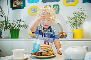 Little curly boy eating sweet pancakes