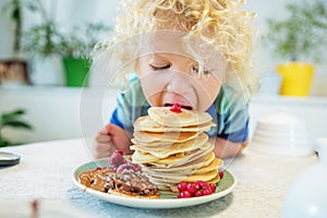 Little curly boy eating sweet pancakes