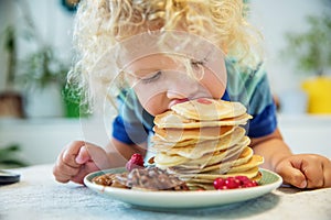 Little curly boy eating sweet pancakes