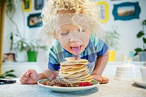 Little curly boy eating sweet pancakes