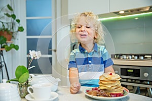 Little curly boy eating sweet pancakes