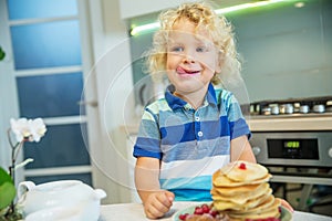 Little curly boy eating sweet pancakes