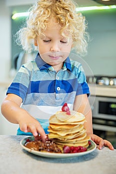 Little curly boy eating sweet pancakes