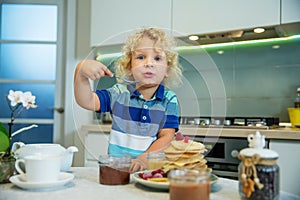 Little curly boy eating sweet pancakes